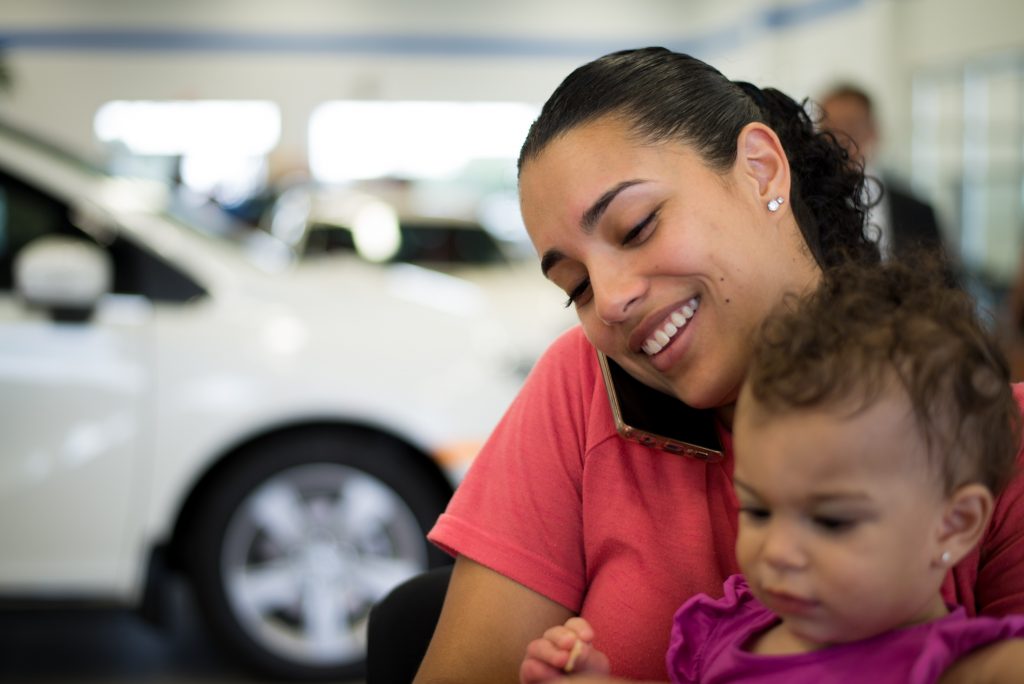 Mom on tthe phone at the dealership with her child